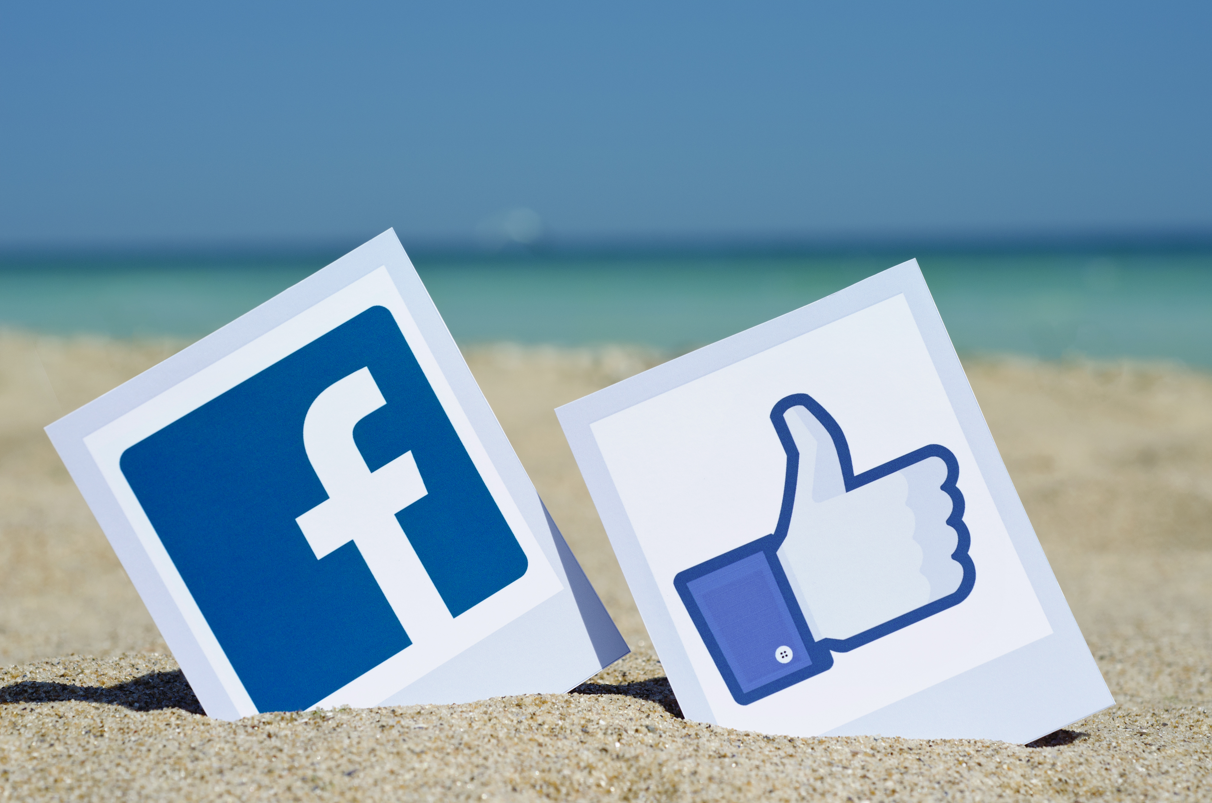 Facebook icons sitting in the sand on a beach with the ocean in the background